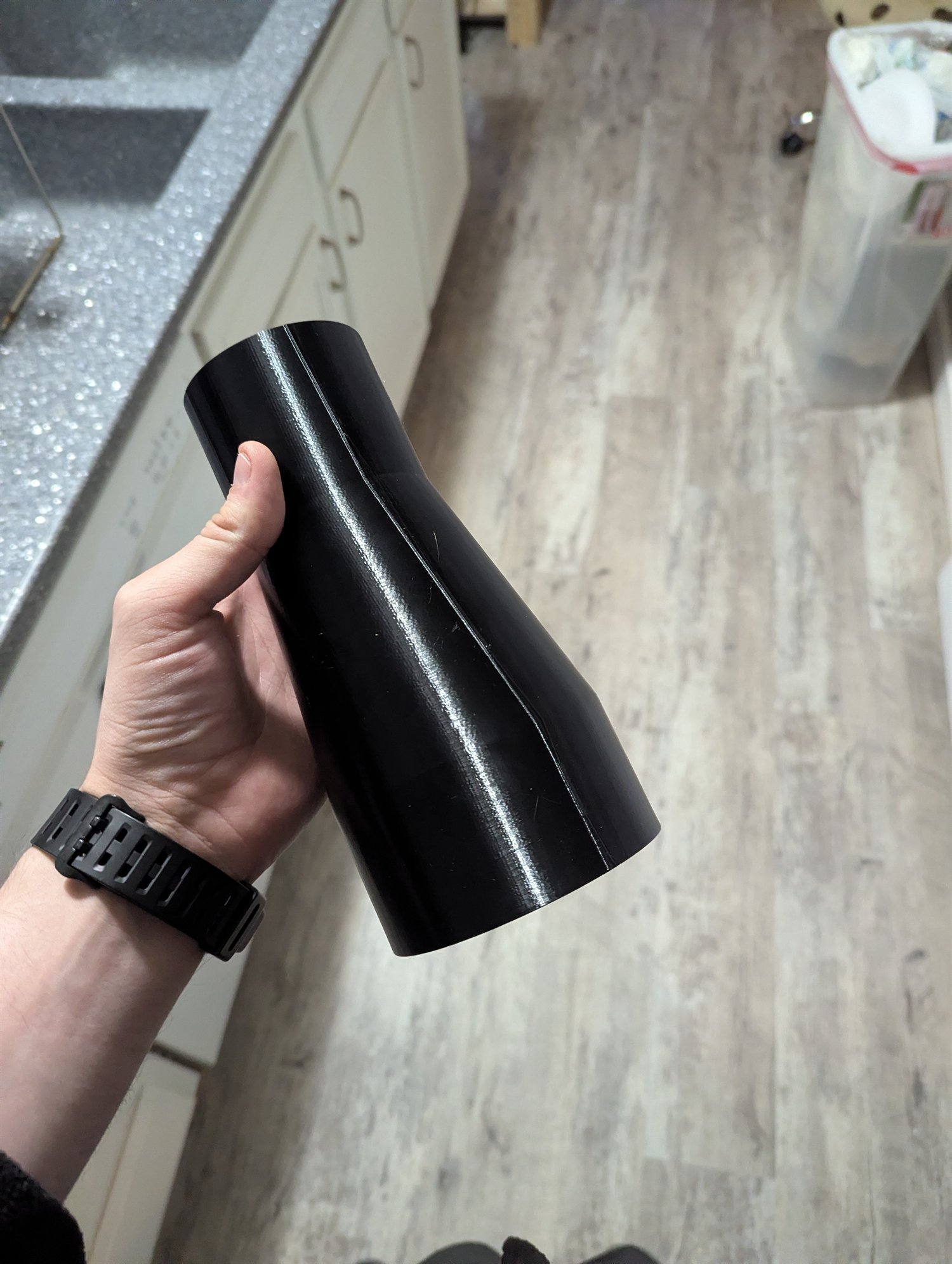 Black 3D-printed CNC machine boot dust cover held in a hand to show its size and contoured shape