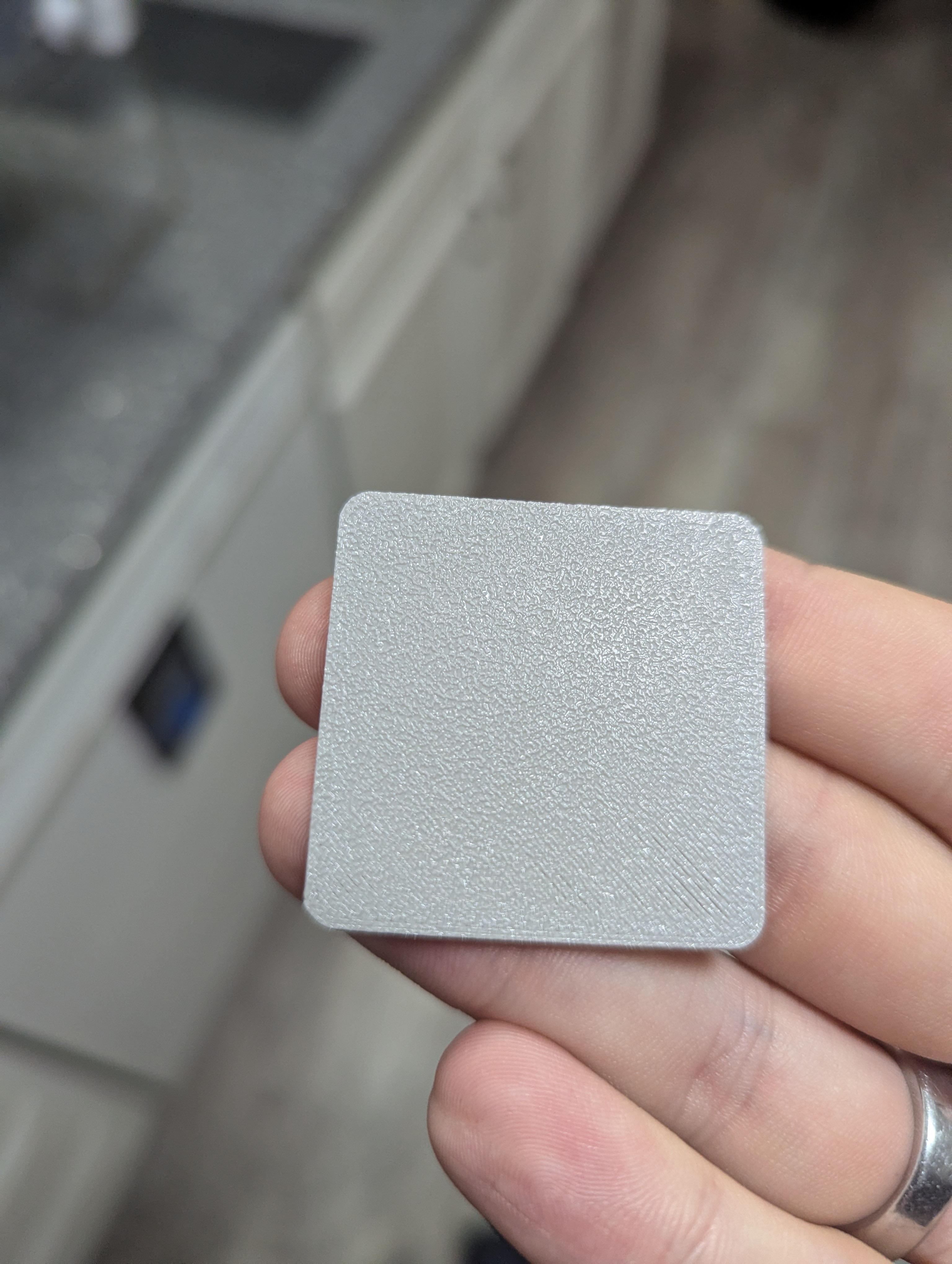Close-up of a square gray 3D printed base plate for a mini figurine