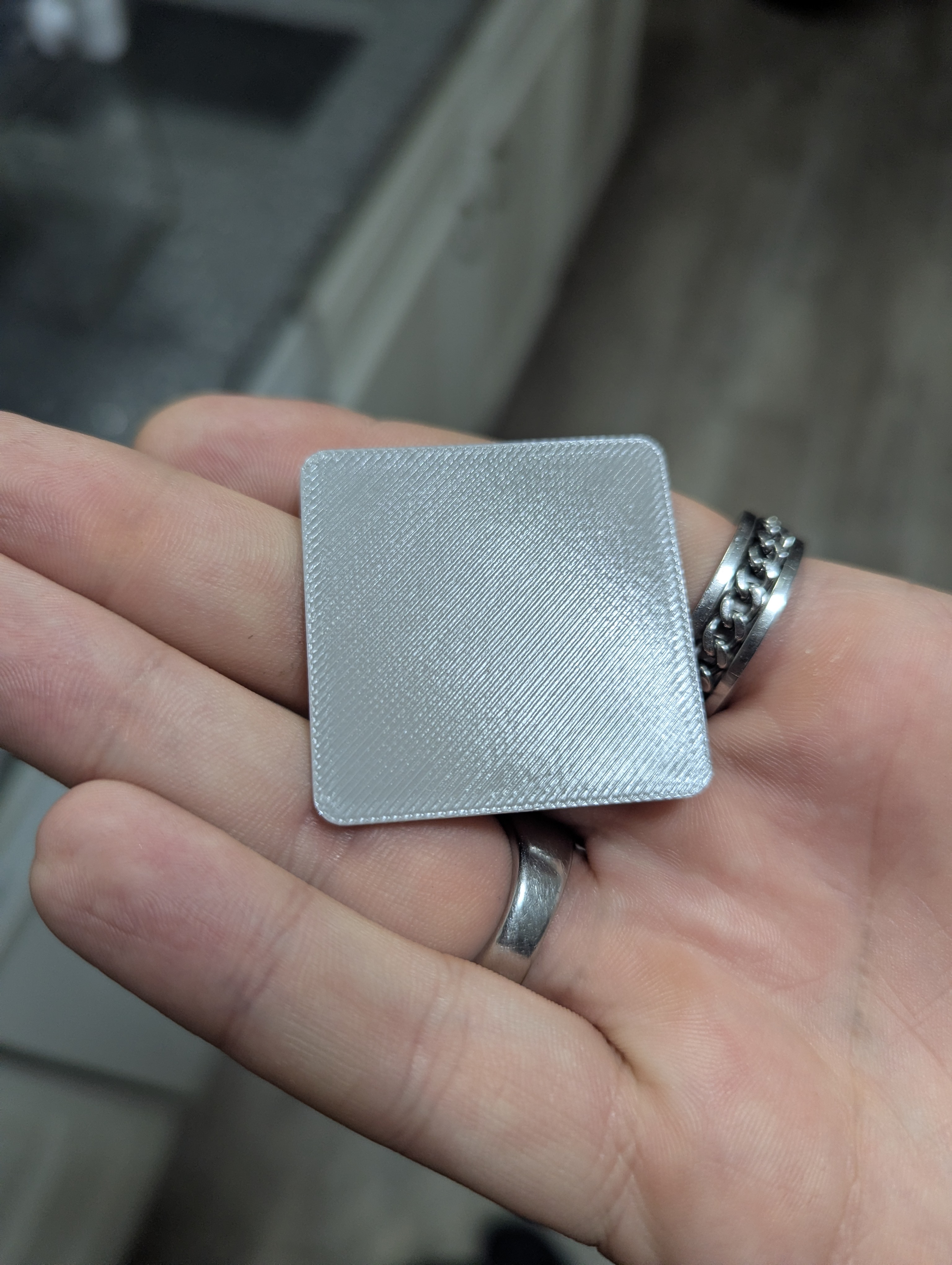 Finished square gray 3D printed mini figurine base plate held in a hand