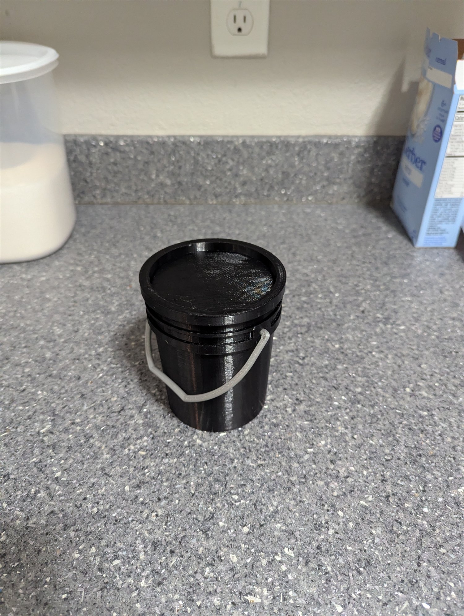 Black 3D-printed miniature five-gallon bucket with its fitted lid and gray handle