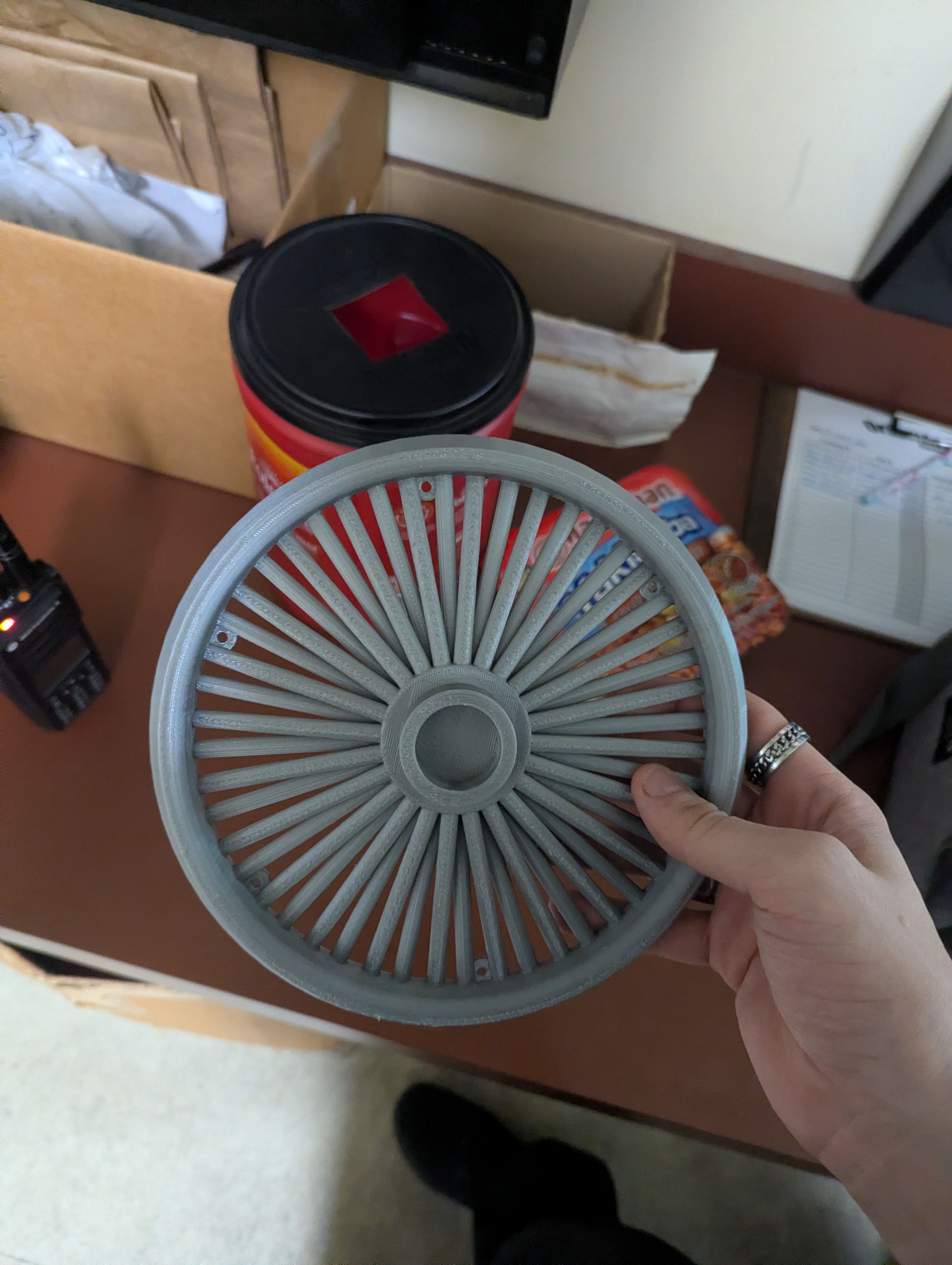 Gray printed trash can wheel cover prototype held up before installation
