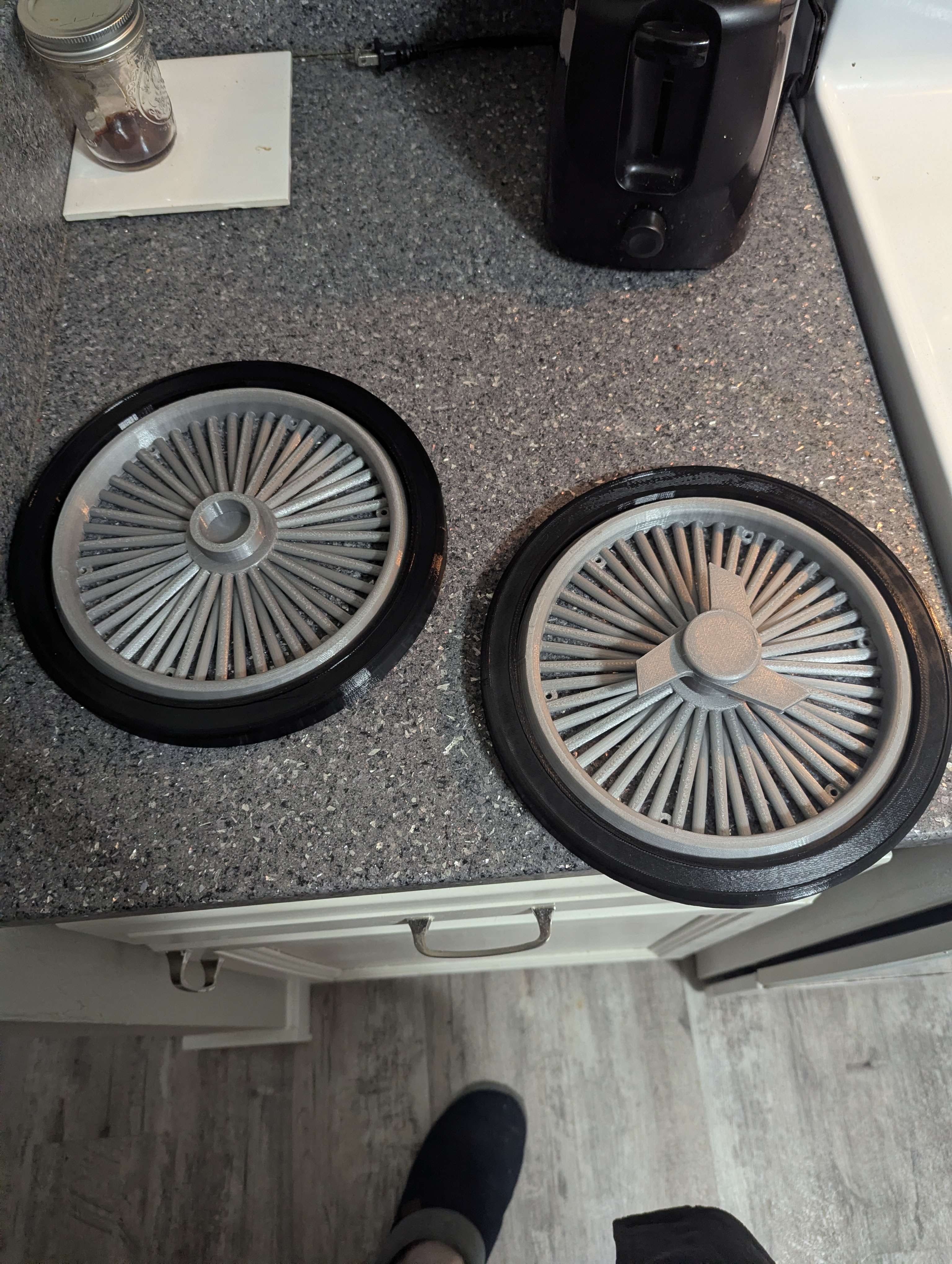 Pair of gray and black printed trash can wheel covers on a countertop